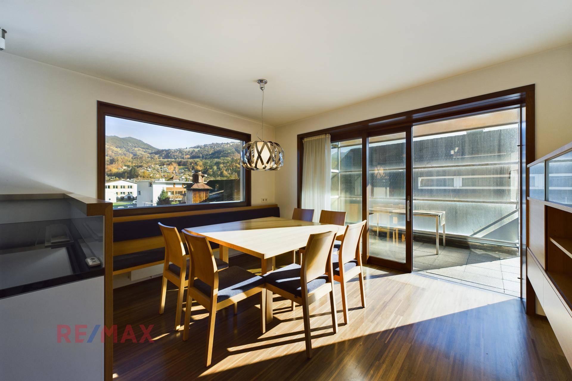 Essbereich mit Holzboden, großem Fenster und direktem Zugang zu einem sonnigen Balkon.