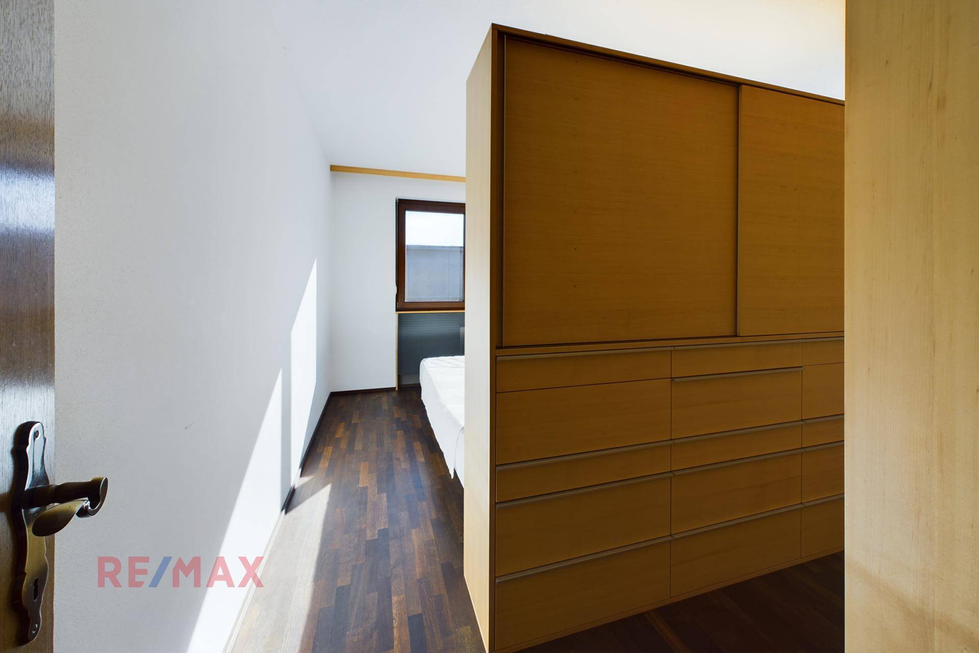 Helles Schlafzimmer mit Holzboden und integriertem Kleiderschrank, gut beleuchtet durch ein Fenster.