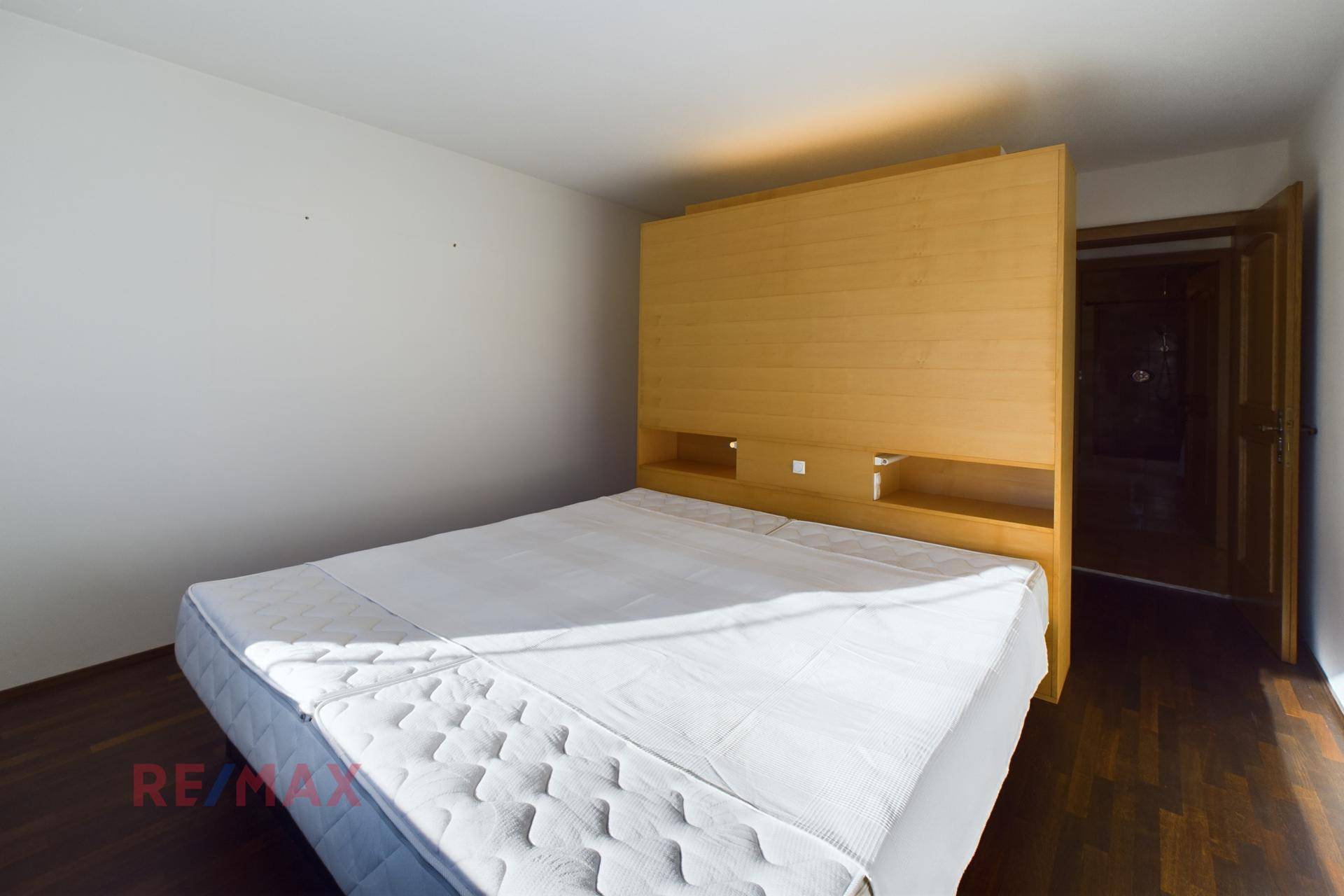 Helles Schlafzimmer mit Holzboden und einem schlichten Bettgestell aus hellem Holz.