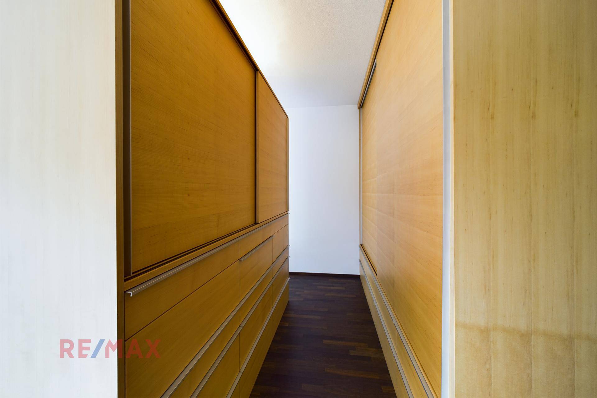 Ankleidebereich mit maßgefertigten Holzschränken und dunklem Holzboden für viel Stauraum.
