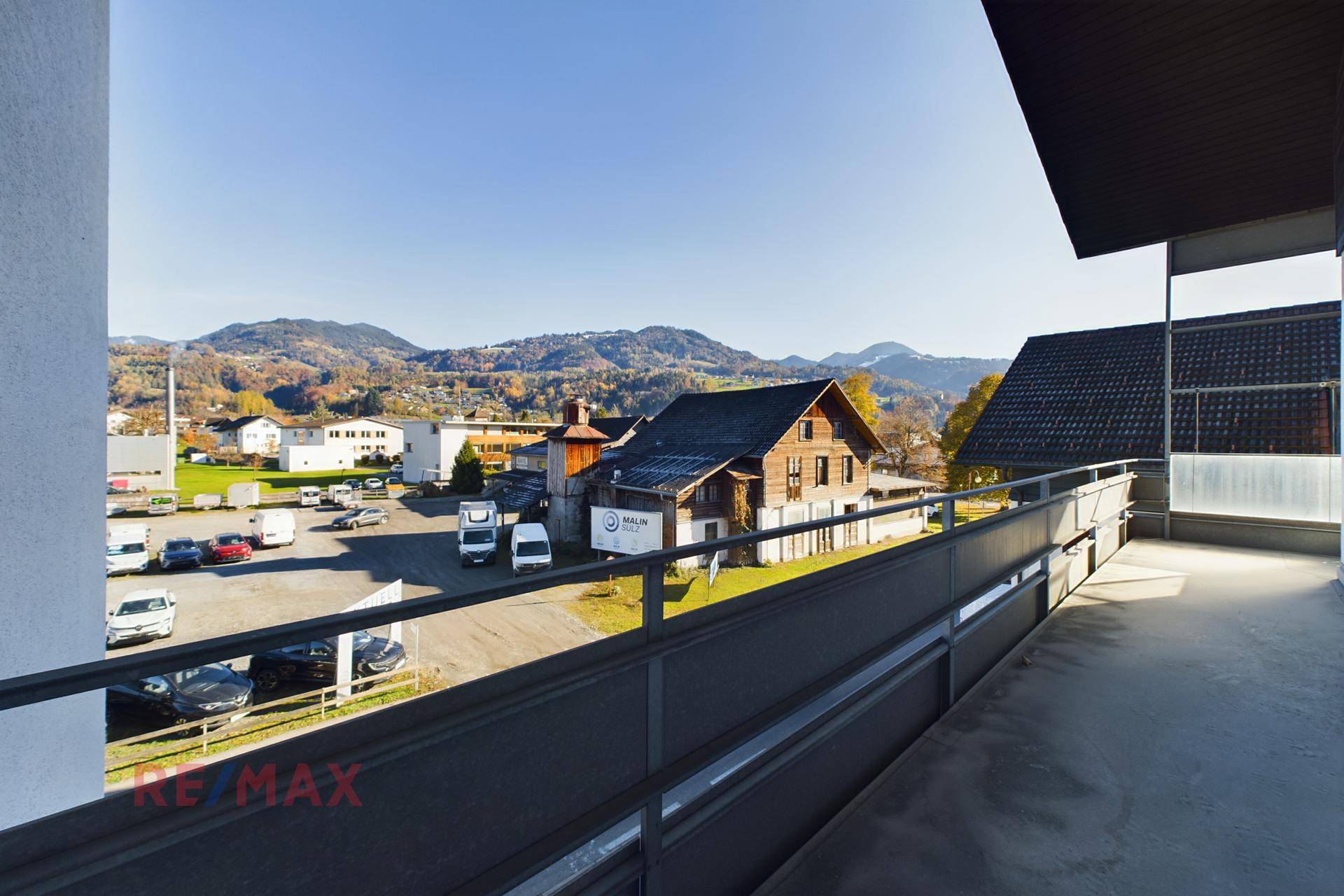 Balkon mit Geländer und weitem Blick über die Dächer und die grüne Landschaft.