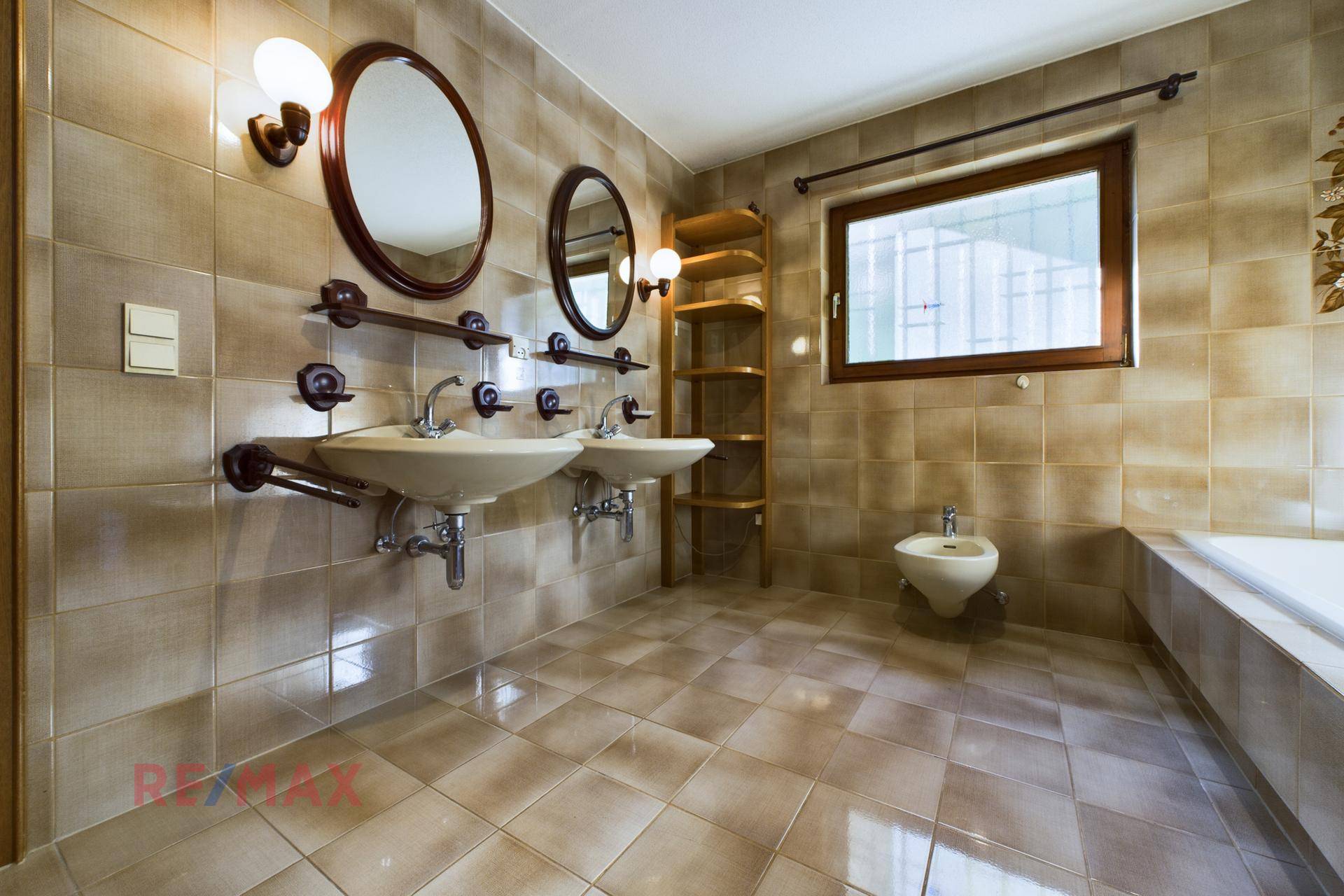 Geräumiges Badezimmer mit beigefarbenen Fliesen, Doppelwaschbecken, Badewanne und Bidet.
