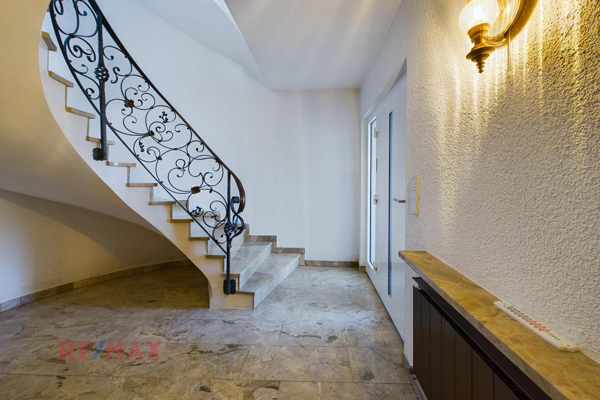 Eleganter Eingangsbereich mit Marmorboden und geschwungener Treppe mit schmiedeeisernem Geländer.