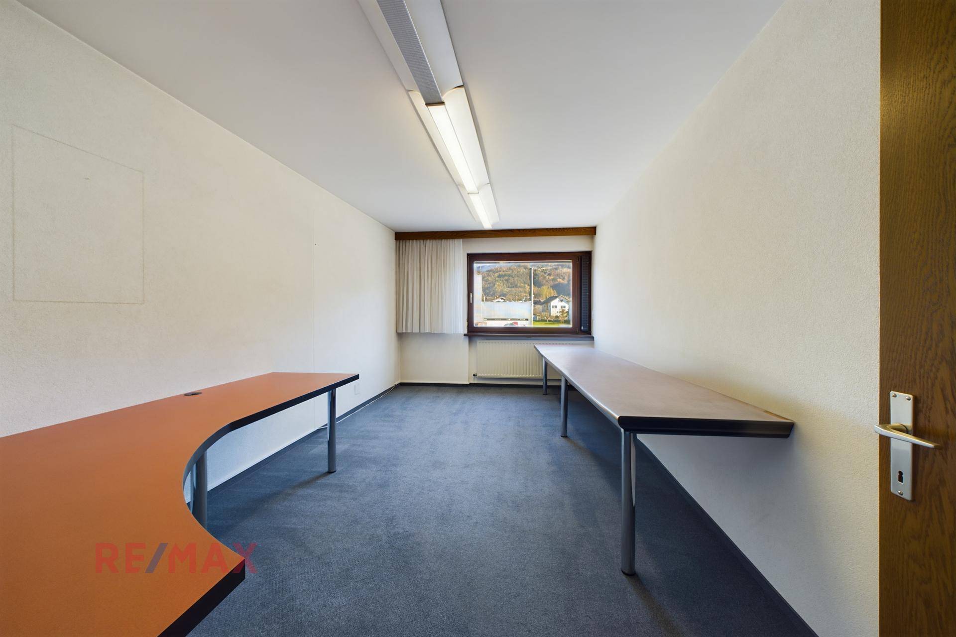 Geräumiges Büro mit Teppichboden und zwei langen Arbeitstischen, ideal für mehrere Arbeitsplätze.