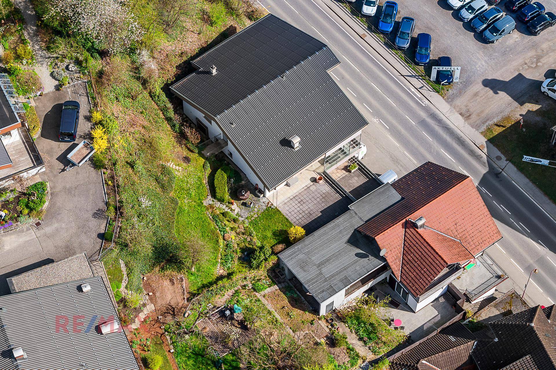 Luftaufnahme des Anwesens mit Garten, Terrasse und umliegender Bebauung unter blauem Himmel.
