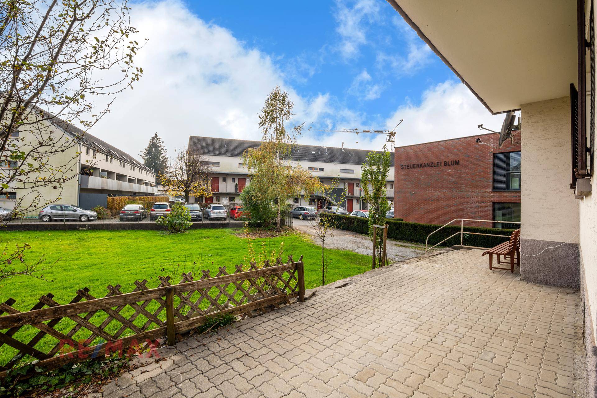 Gepflasterte Terrasse mit Holzzaun und Blick auf die umliegenden Gebäude und Parkplätze.