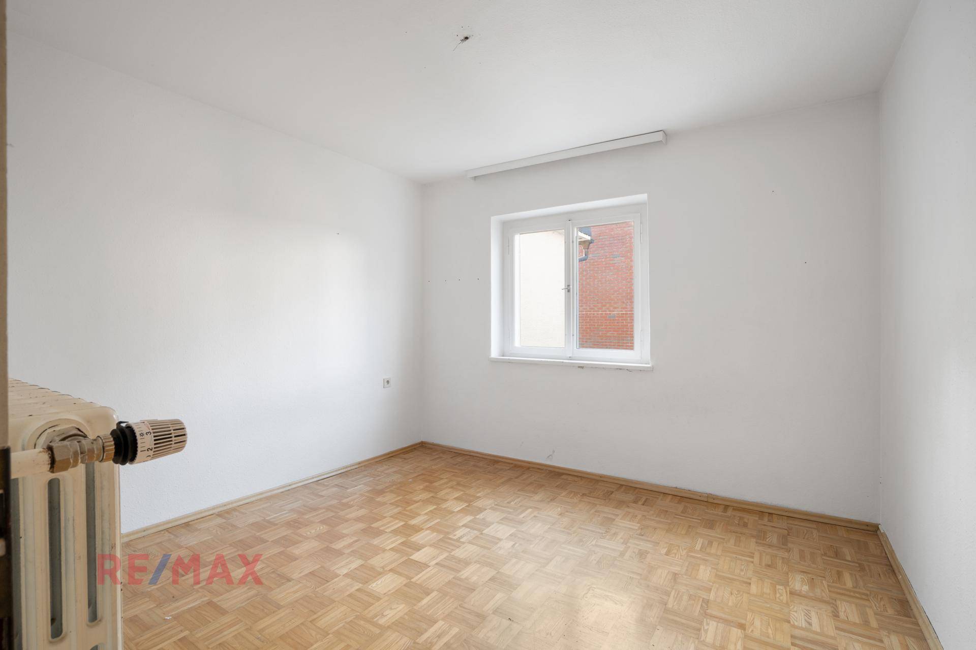Helles Zimmer mit Parkettboden und Heizkörper unter dem Fenster.