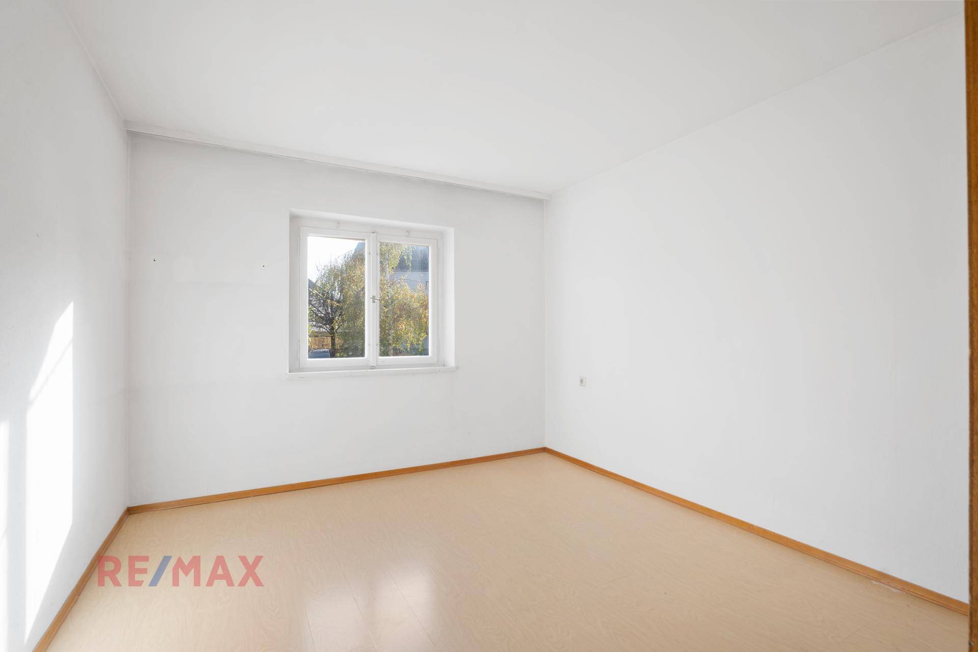 Geräumiges Zimmer mit hellem Bodenbelag und Fenster mit Blick ins Grüne.