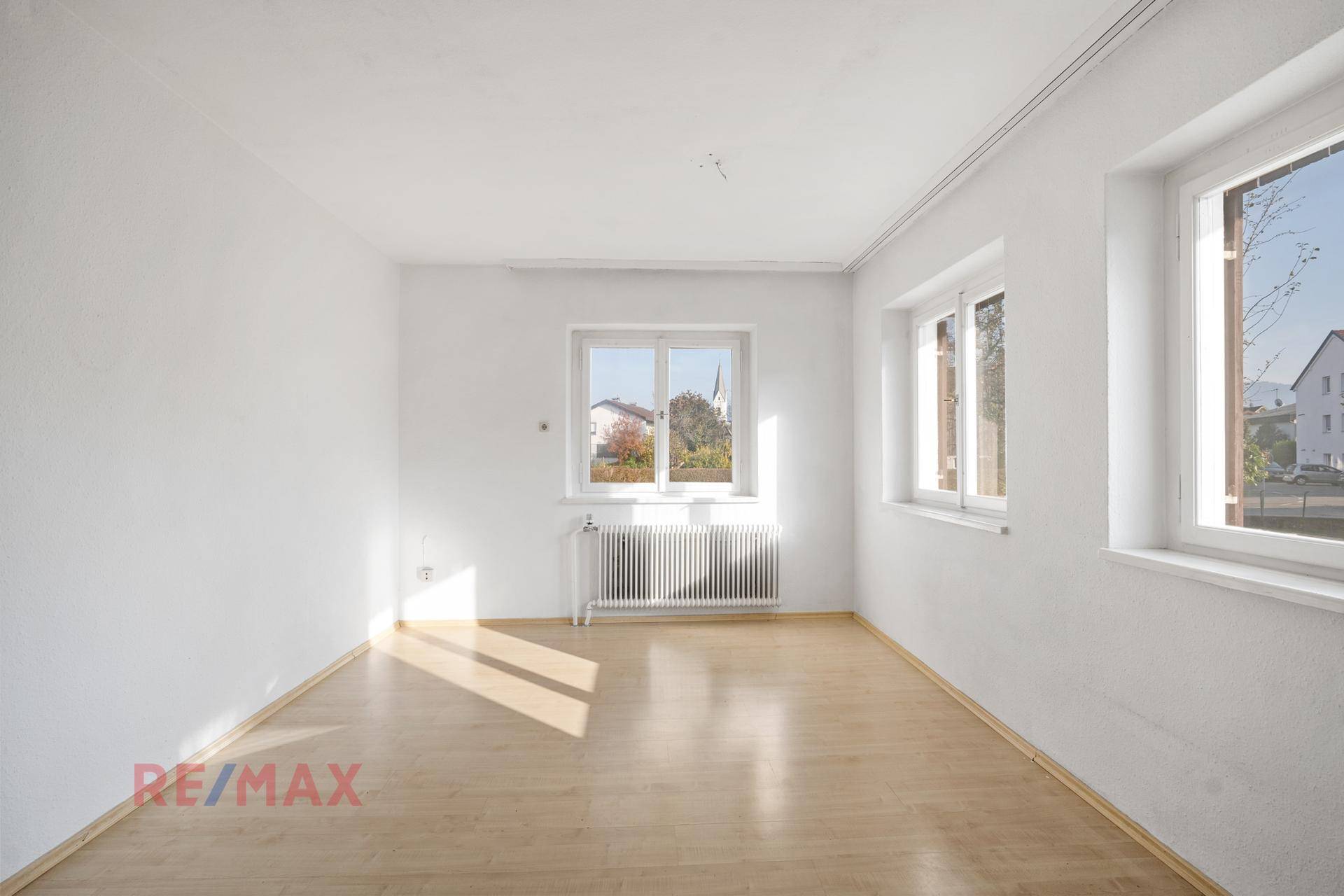 Lichtdurchflutetes Wohnzimmer mit Laminatboden und mehreren Fenstern.