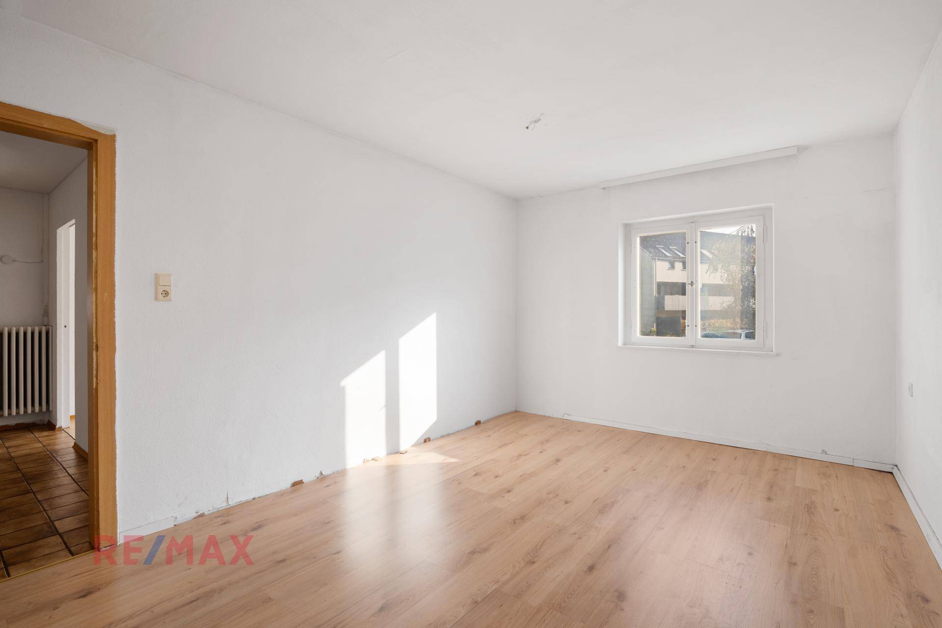 Helles Zimmer mit Laminatboden und sonnigem Lichteinfall durch das Fenster.