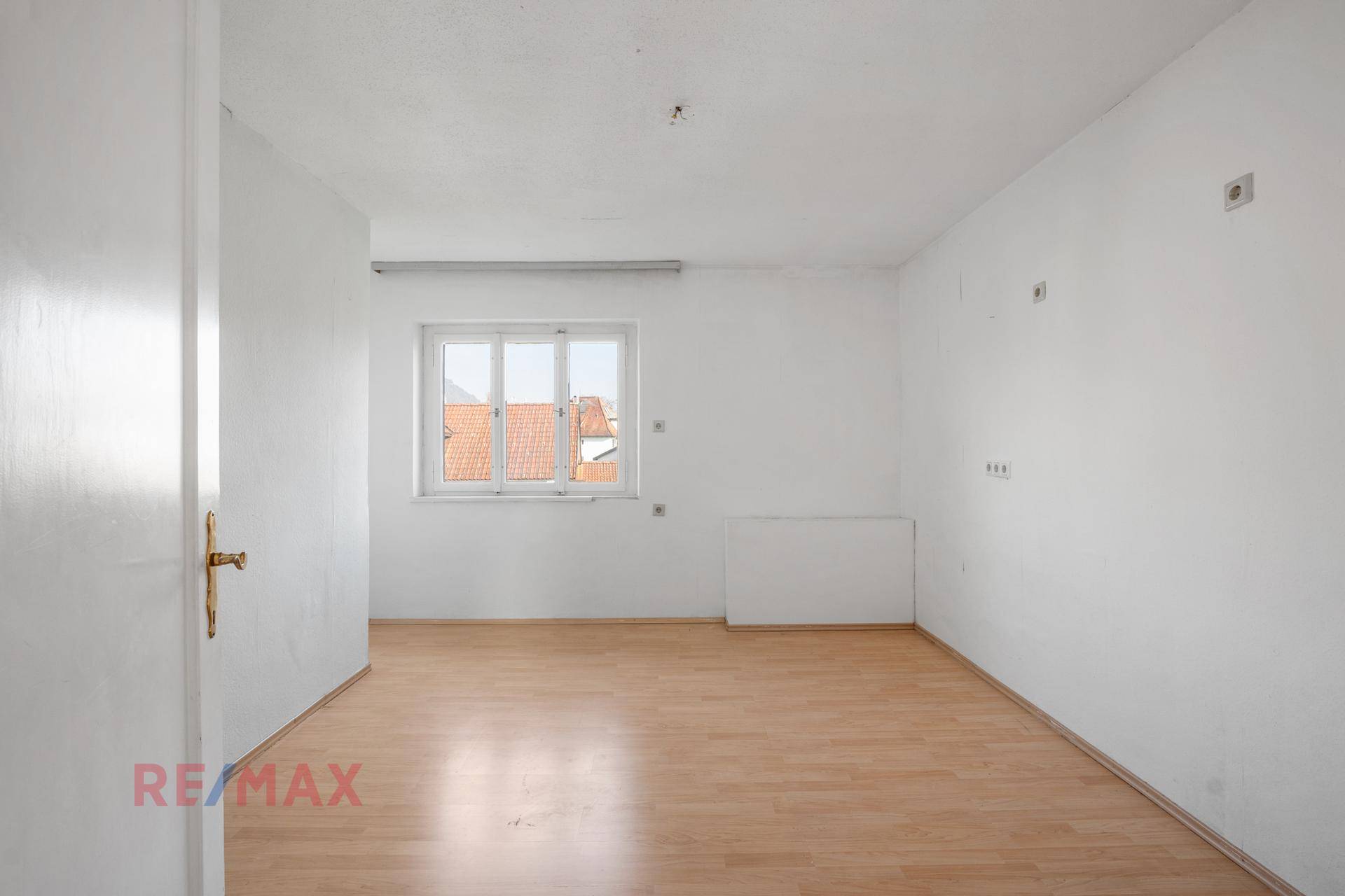 Helles Zimmer mit Laminatboden und Fenster mit Blick auf die Dächer.