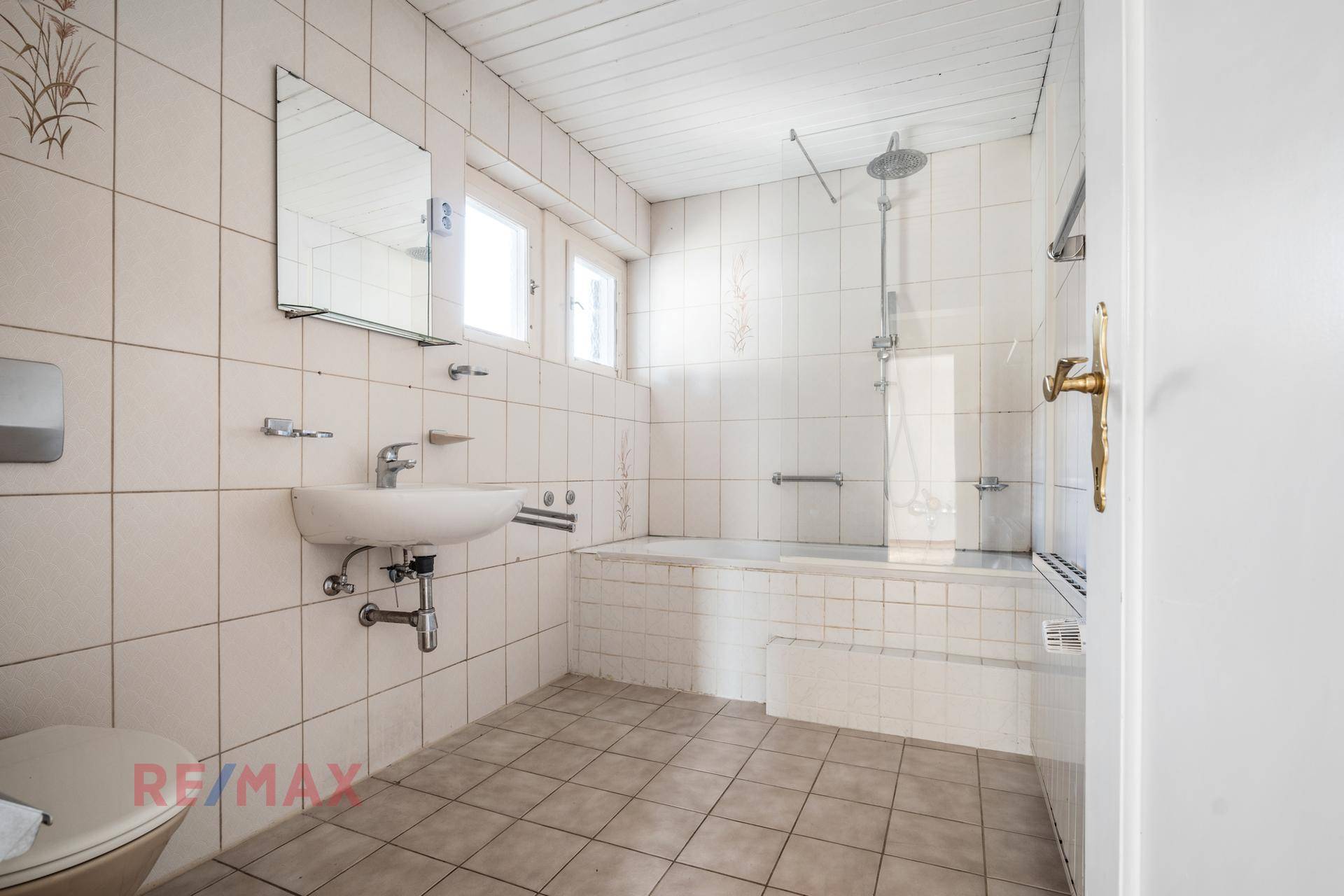 Gefliestes Badezimmer mit Badewanne, Dusche und Fenster für Tageslicht.