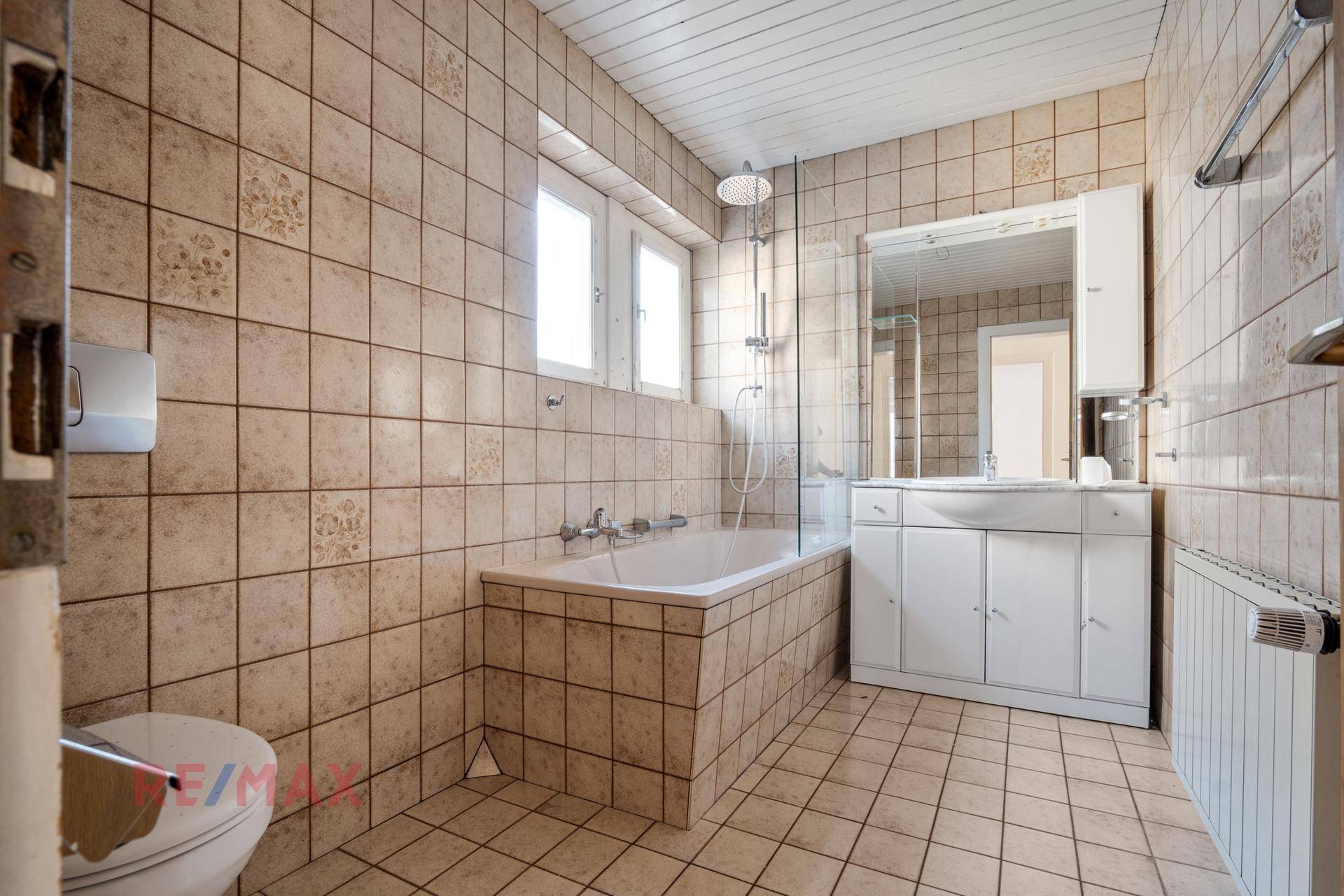Badezimmer mit beigefarbenen Fliesen, Badewanne und Waschtisch mit Spiegelschrank.