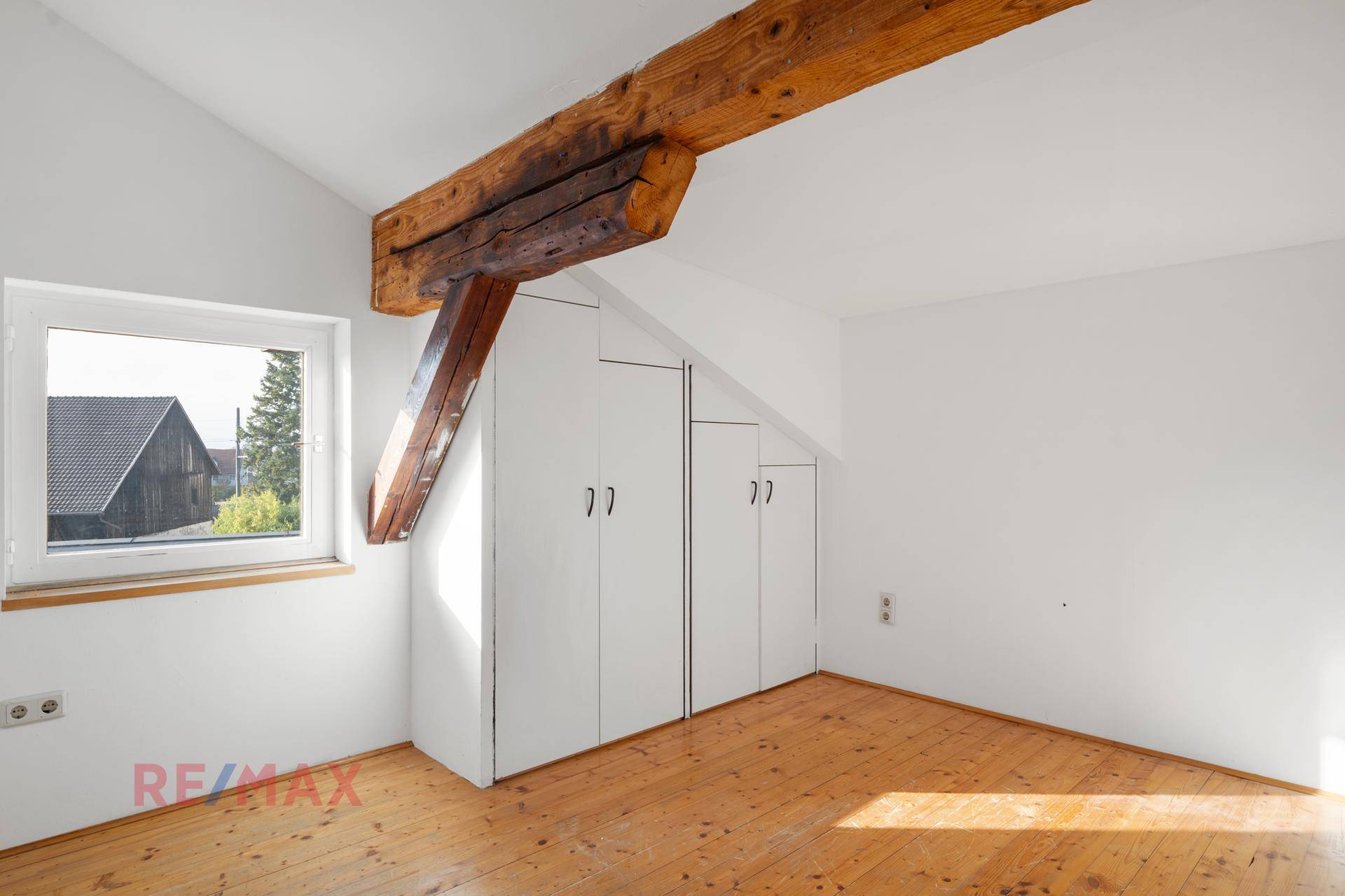 Ausgebautes Dachzimmer mit Holzbalken, Einbauschränken und Holzdielenboden.