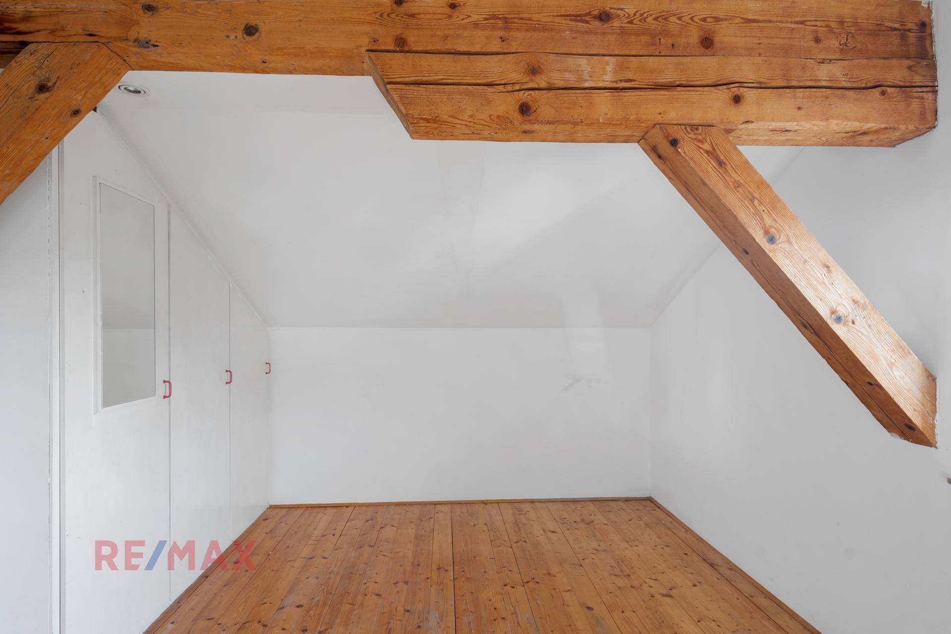 Helles Dachzimmer mit Holzbalken und Holzdielenboden.