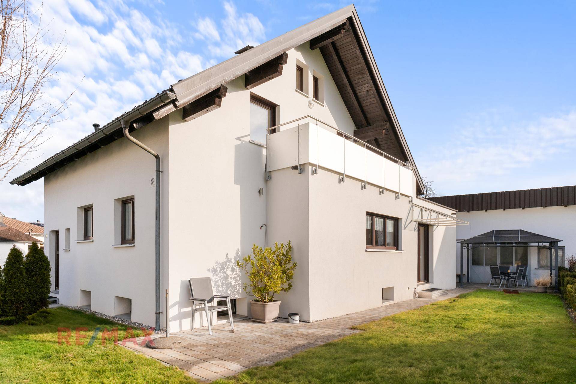 Rückseite des Hauses mit Rasenfläche, kleiner Terrasse und Balkon im Obergeschoss.