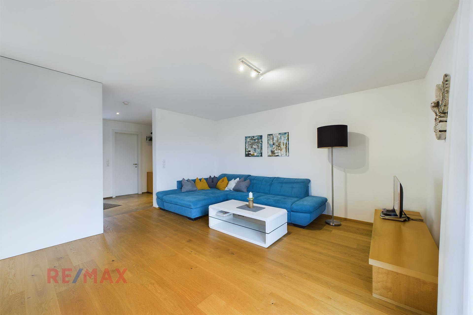 Geräumiges Wohnzimmer mit blauem Sofa, hellem Holzboden und moderner Dekoration.