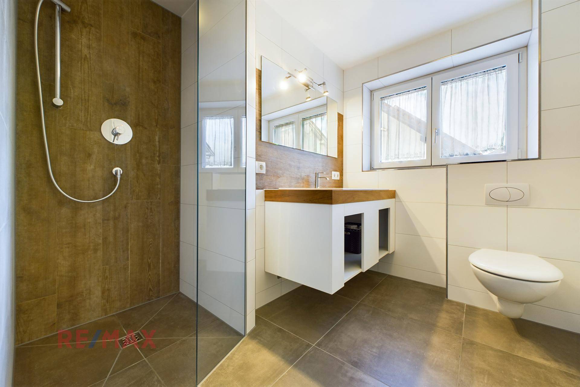 Modernes Badezimmer mit ebenerdiger Dusche, Holzdetails und Fenster für Tageslicht.