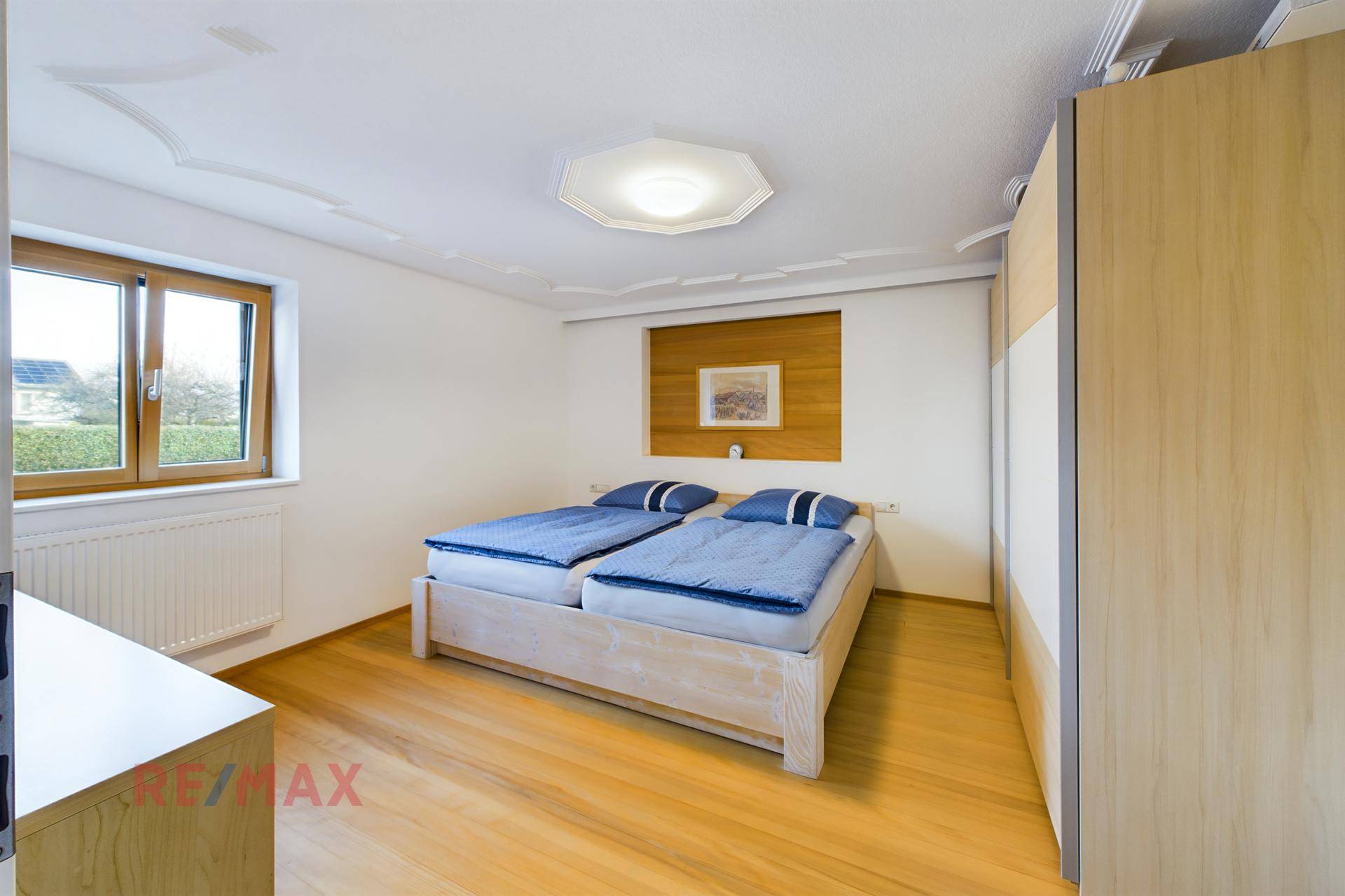 Helles Schlafzimmer mit Doppelbett, Holzschrank und dekorativer Decke.
