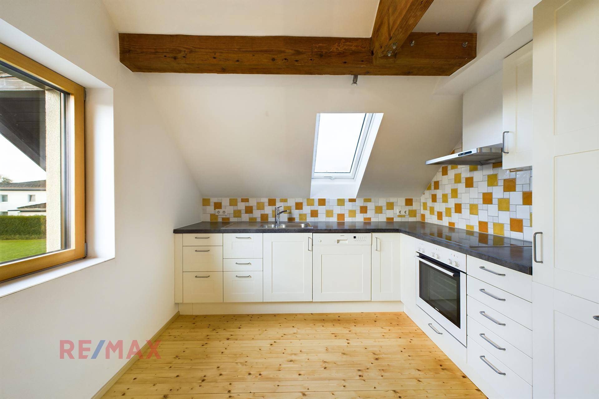 Küche im Dachgeschoss mit Dachfenster, Holzbalken und farbigen Fliesen als Spritzschutz.