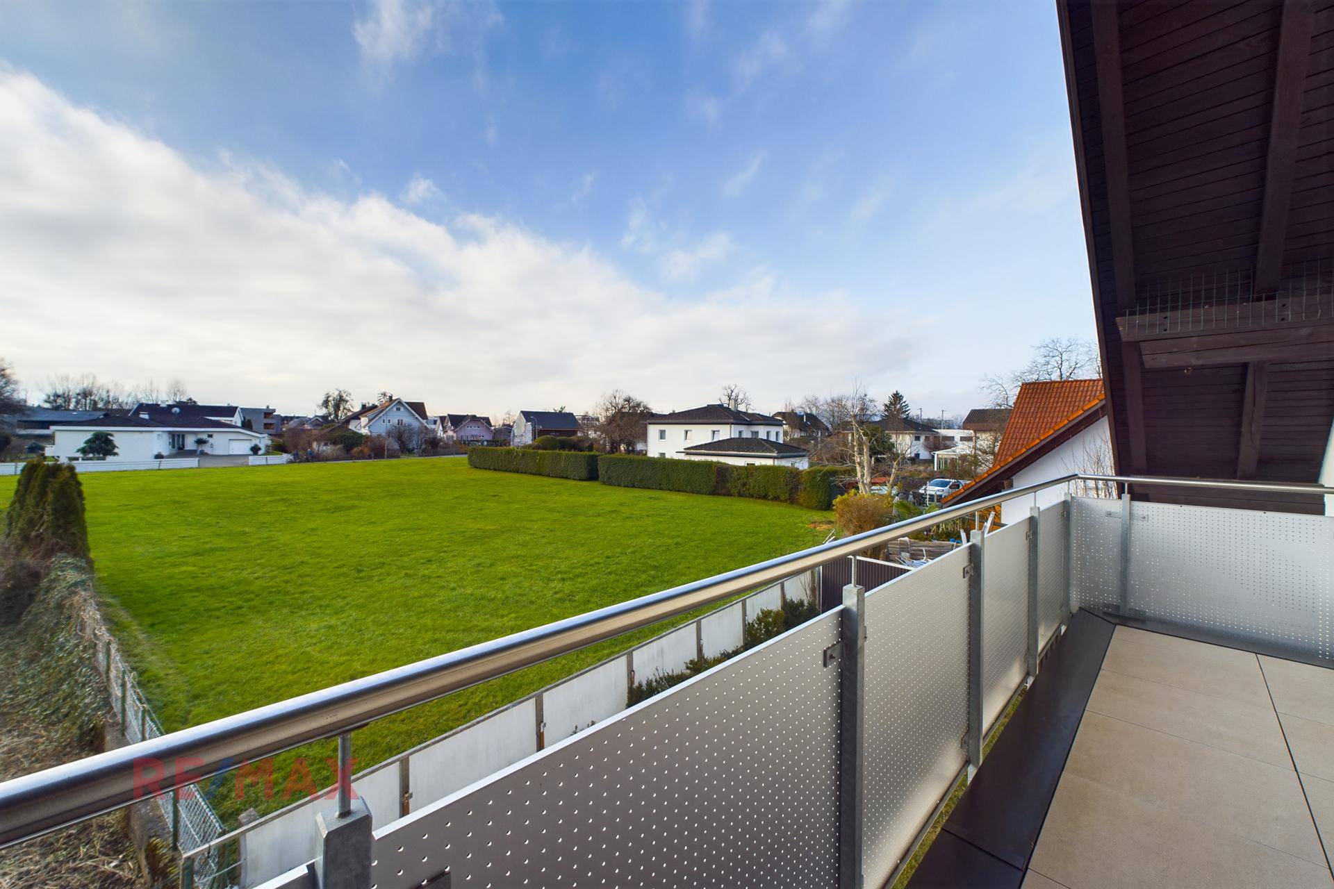 Balkon mit Metallgeländer und weitem Blick über grüne Wiesen und Häuser.