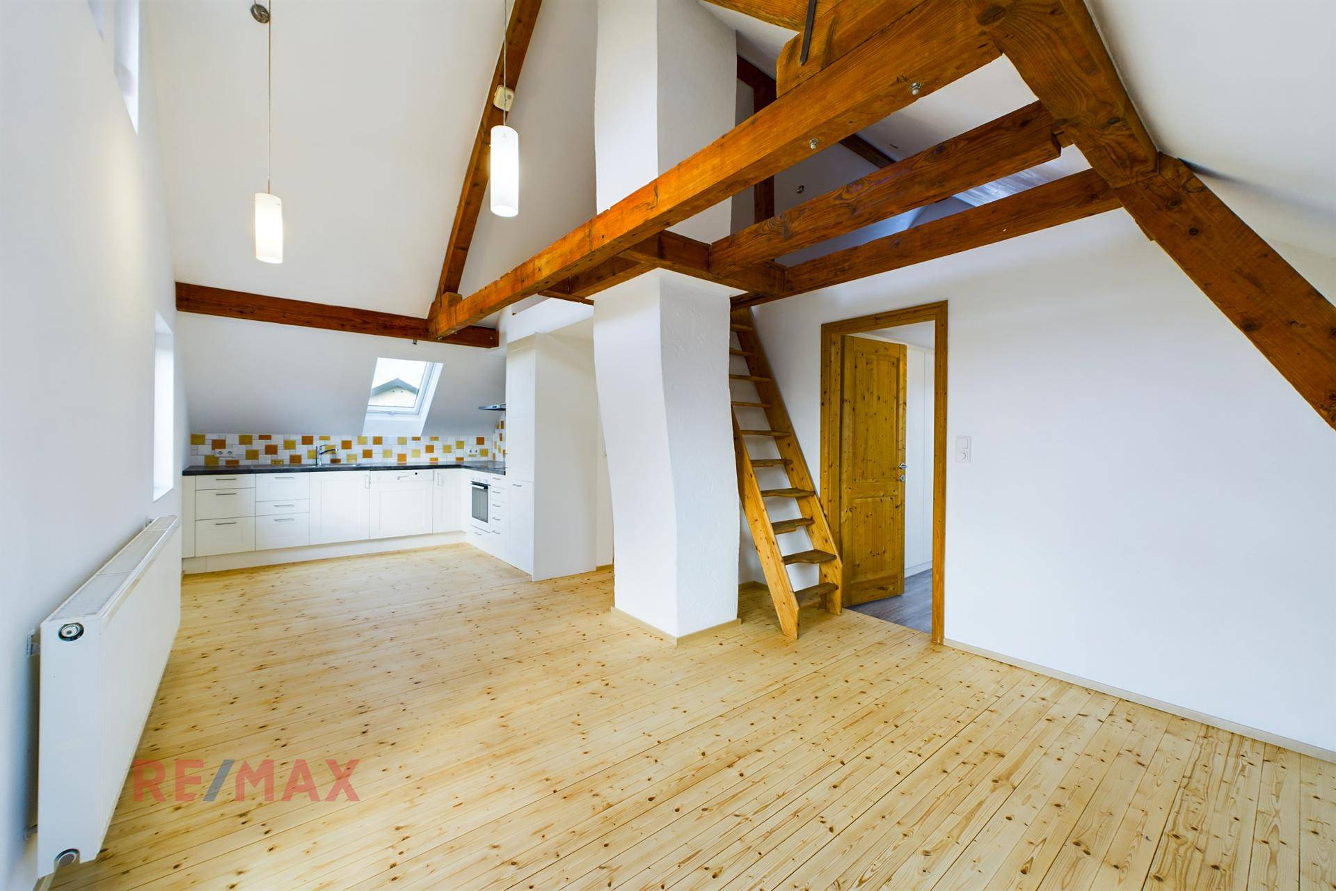 Geräumiger Wohnbereich im Dachgeschoss mit sichtbaren Holzbalken und offener Treppe.