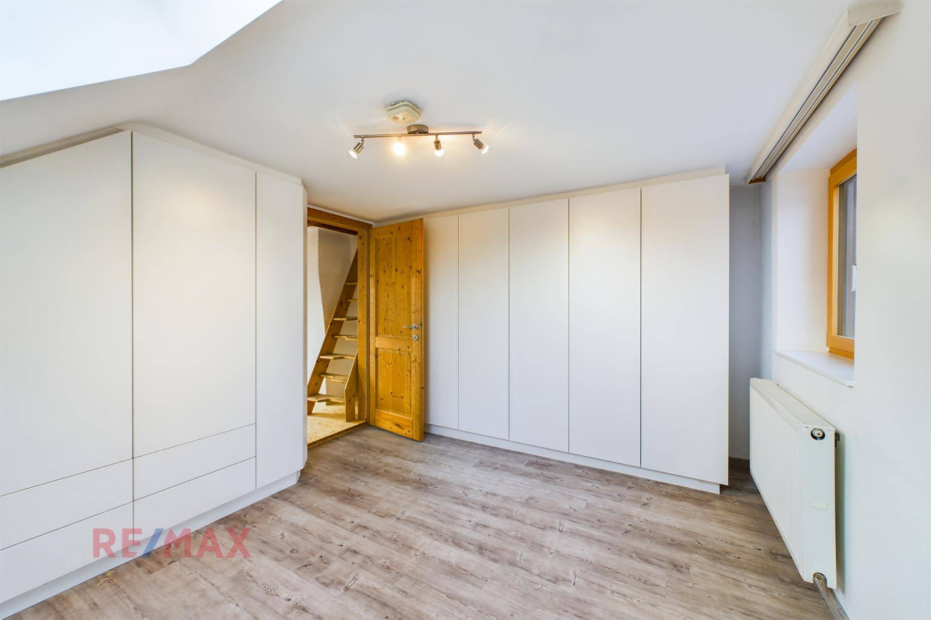 Dachgeschosszimmer mit Einbauschränken, Heizkörper und Laminatboden.