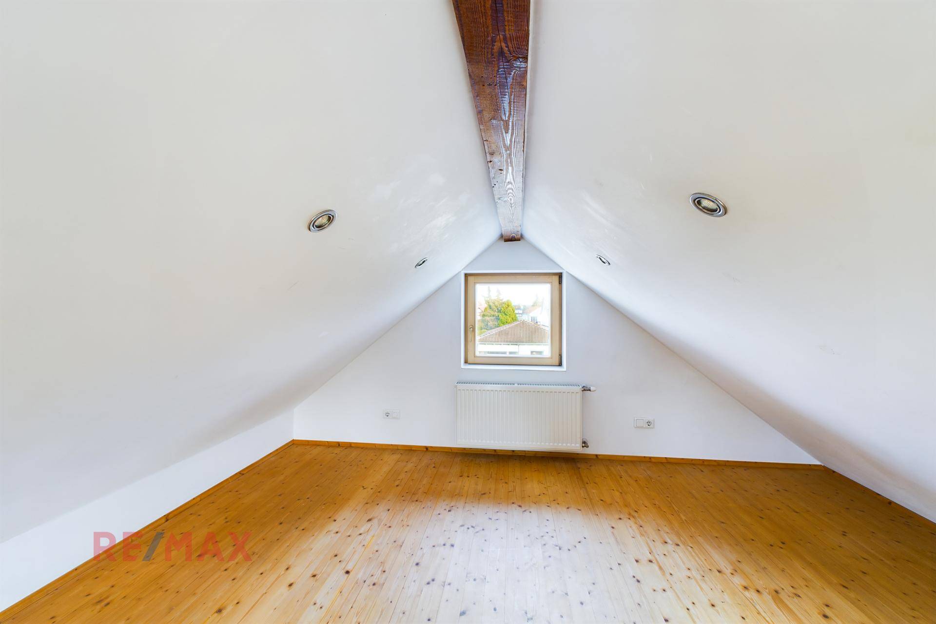 Leeres Dachbodenzimmer mit Holzbalken, Fenster und hellem Holzfußboden.