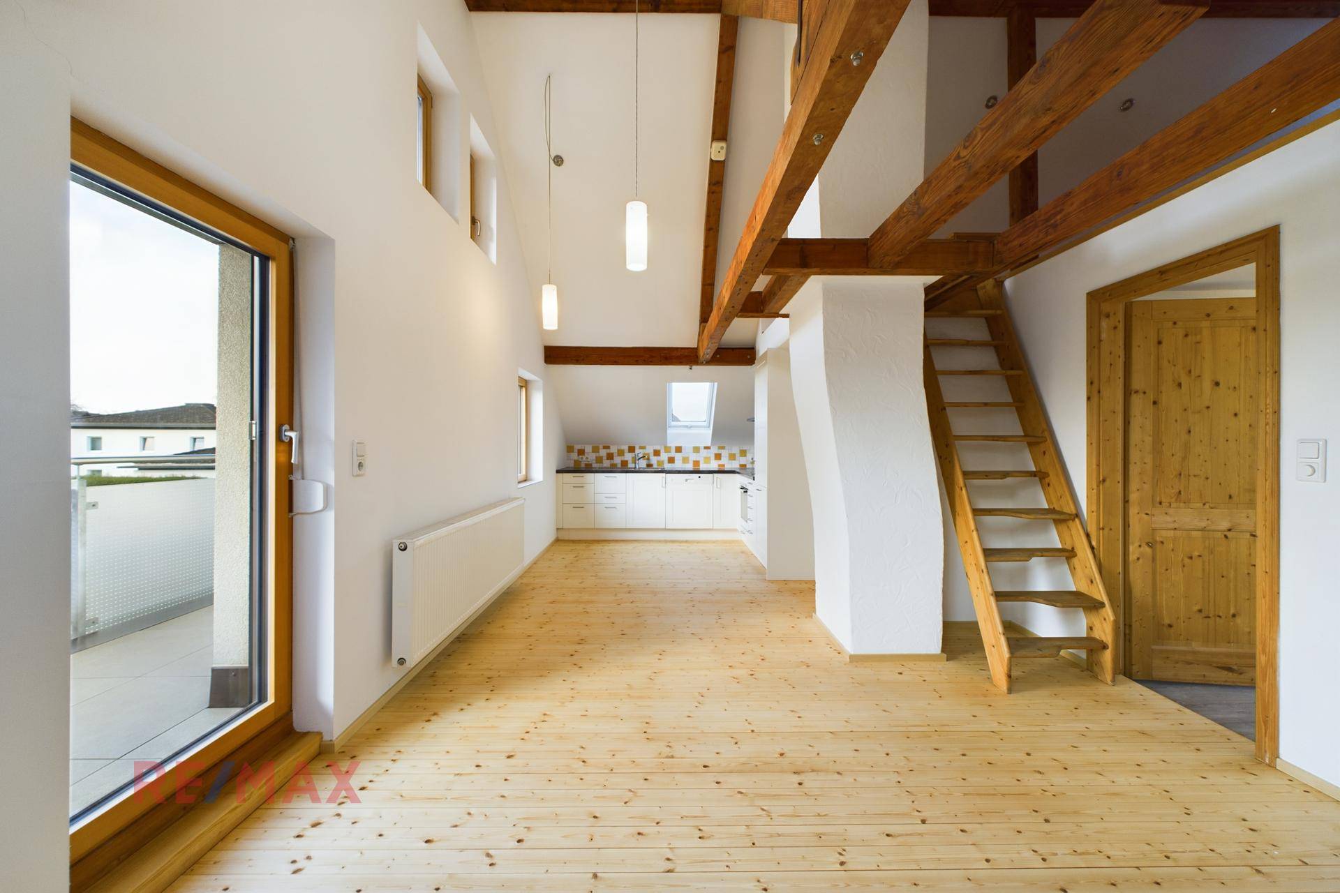 Offener Wohnbereich im Dachgeschoss mit hohen Decken, Holzbalken und Balkonzugang.