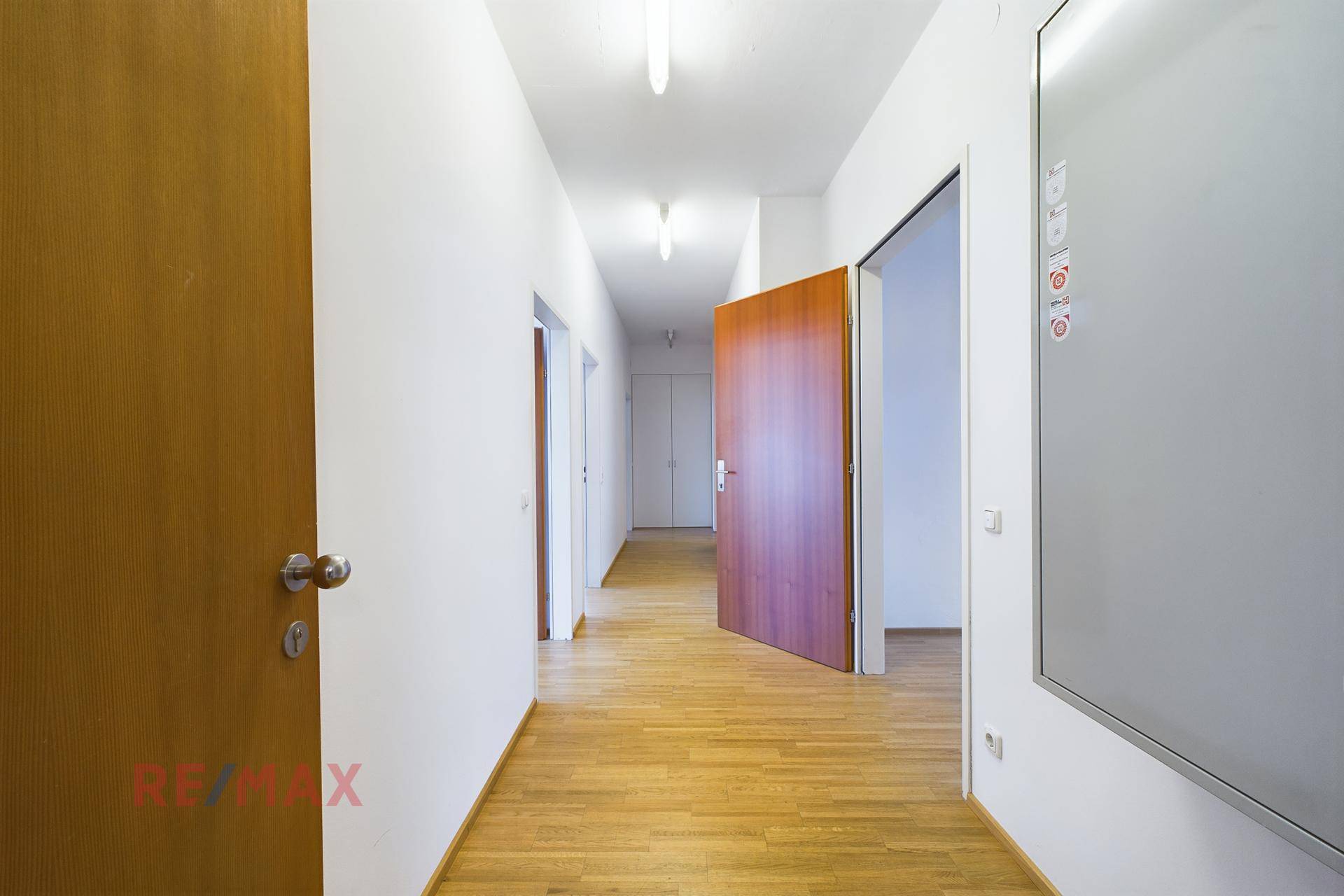Flur mit Holzboden und Holztüren, der zu weiteren Büroräumen und einem Whiteboard führt.