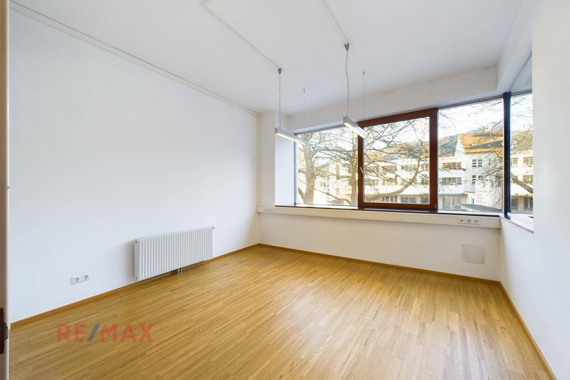 Heller Büroraum mit großen Fenstern, die viel Tageslicht hereinlassen, und Holzboden.