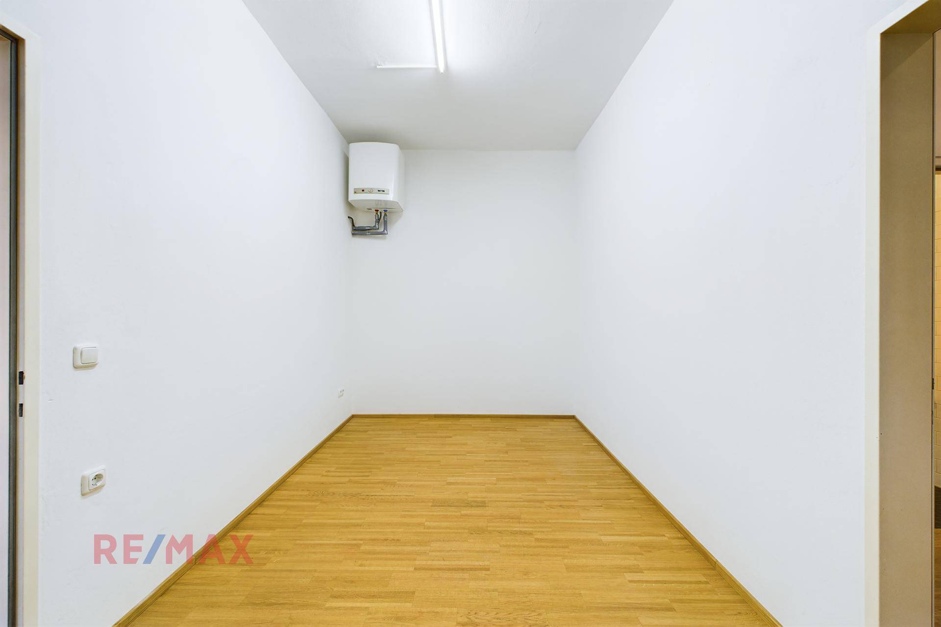 Kleiner Abstellraum oder Technikraum mit einem Warmwasserbereiter an der Wand und Holzboden.