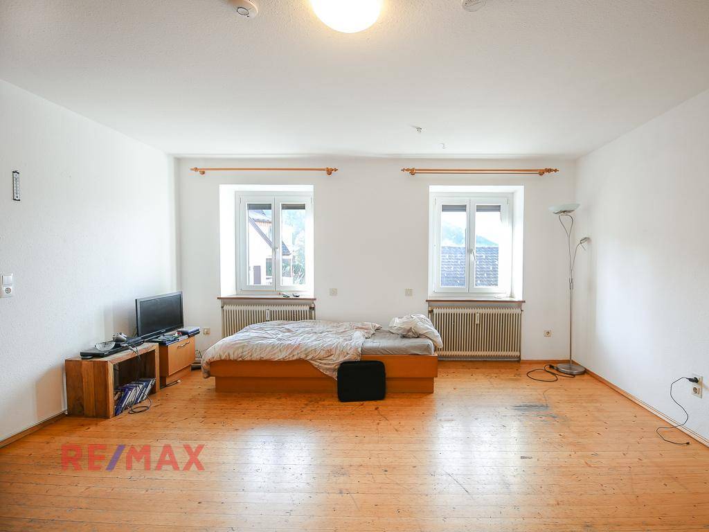 Helles Schlafzimmer mit Holzboden, zwei Fenstern und einem einfachen Bett, mit Bergblick.