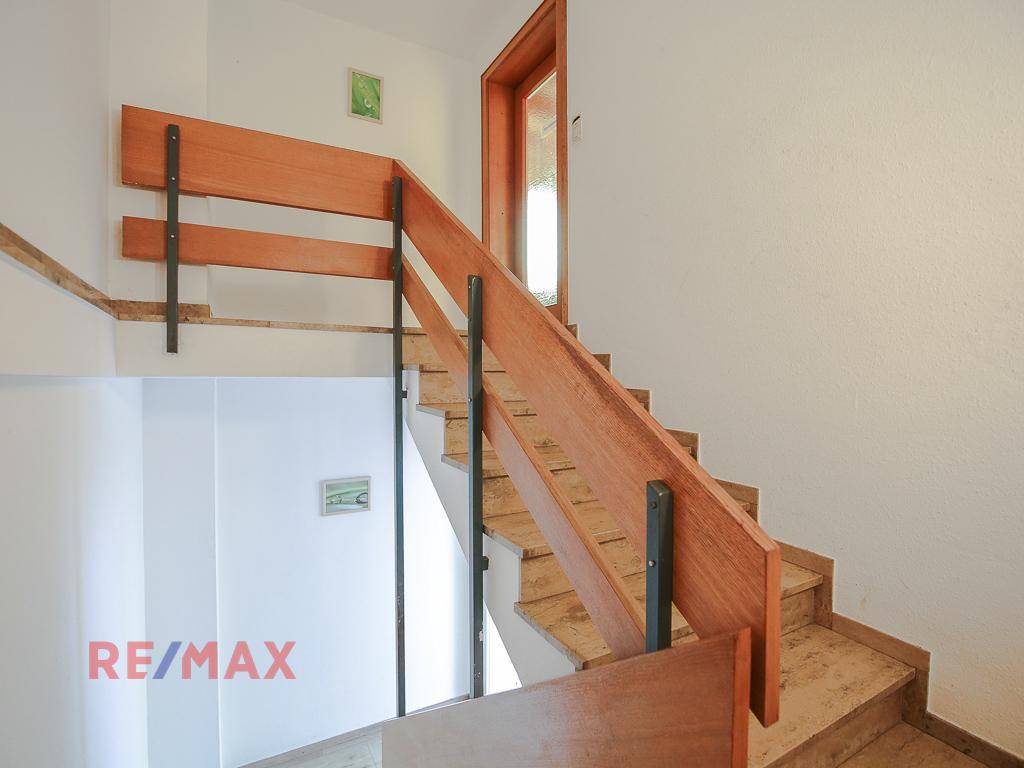 Treppenhaus mit Holzgeländer und gefliesten Stufen, das die Etagen verbindet.