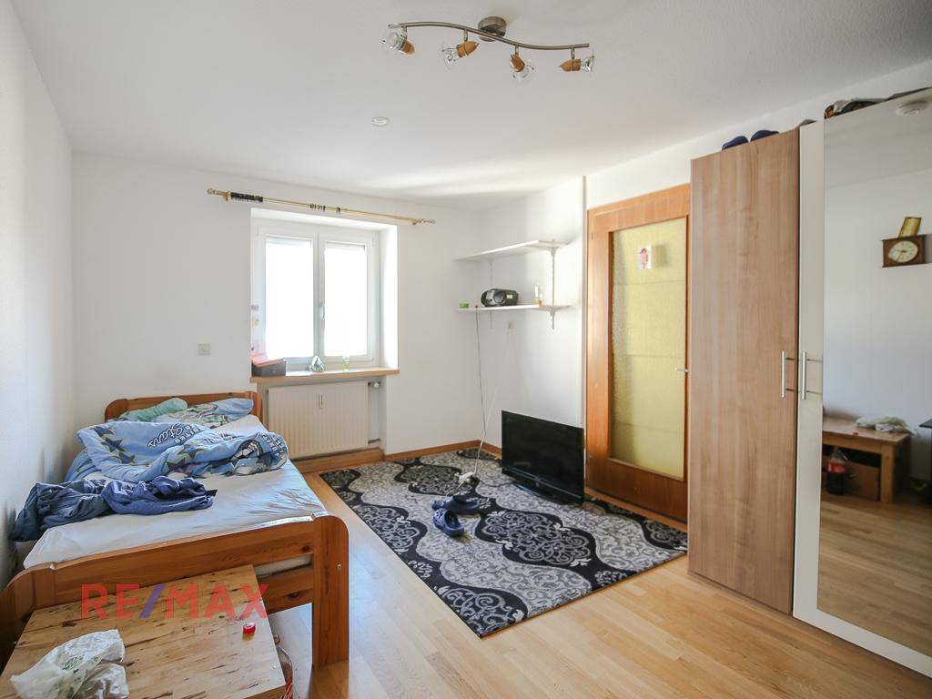 Schlafzimmer mit Holzboden, Fenster und einem Kleiderschrank mit Spiegeltür.