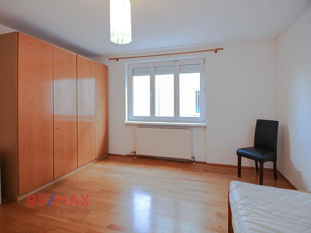 Schlafzimmer mit Holzboden, großem Fenster und einem geräumigen Holzschrank.