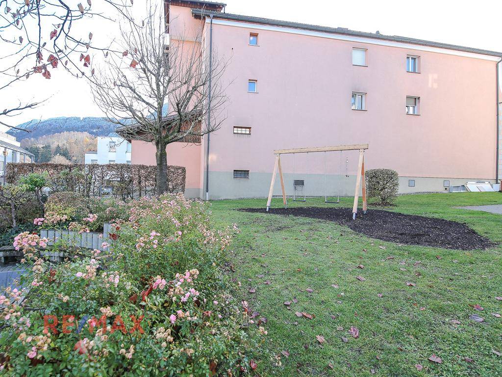 Grüner Gartenbereich mit Schaukel und Rosenbeeten hinter dem Gebäude.