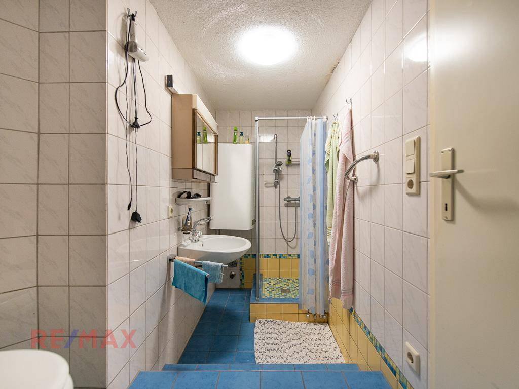 Badezimmer mit Dusche, Waschbecken und farbigen Fliesen in Blau und Gelb.