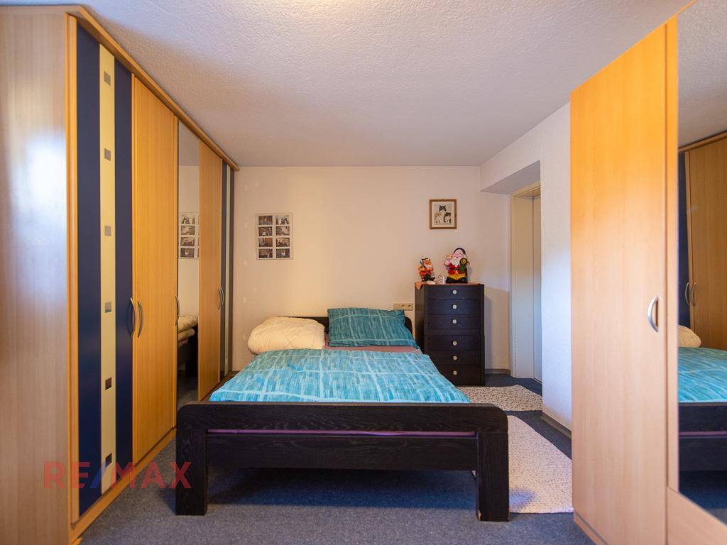 Schlafzimmer mit Teppichboden, großem Kleiderschrank mit Spiegeltüren und Einzelbett.