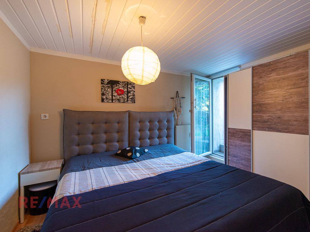 Schlafzimmer mit Doppelbett, Holzwänden an der Decke und Zugang zu einem kleinen Balkon.