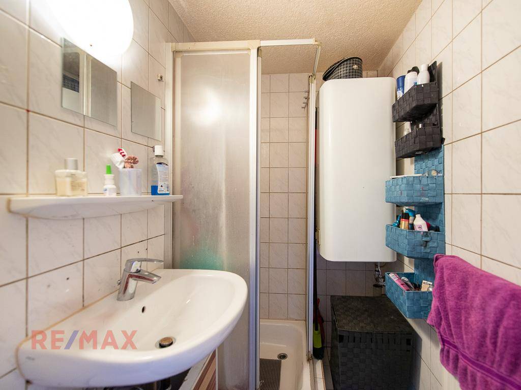 Kleines Badezimmer mit Duschkabine, Waschbecken und weißen Wandfliesen.