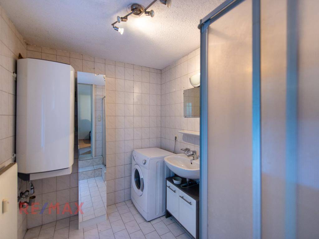 Badezimmer mit Dusche, Waschbecken und Waschmaschine, gefliest in hellen Farben.