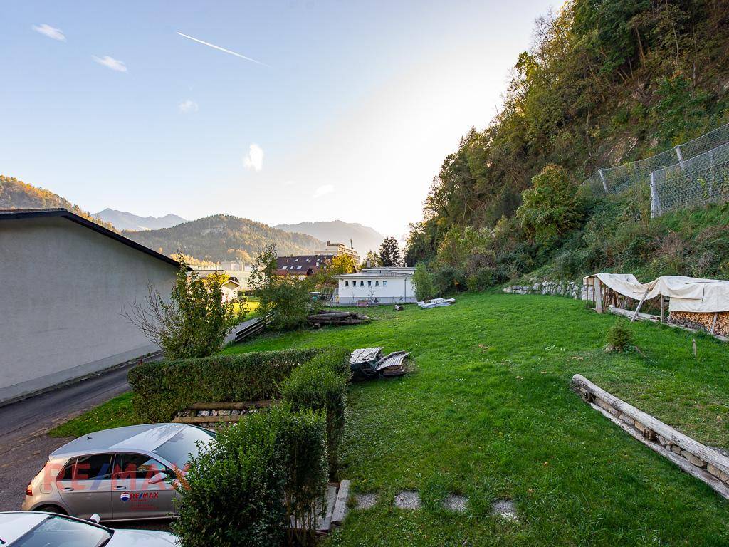 Panoramablick auf die grüne Umgebung mit Bergen, Häusern und einem weiten Himmel.