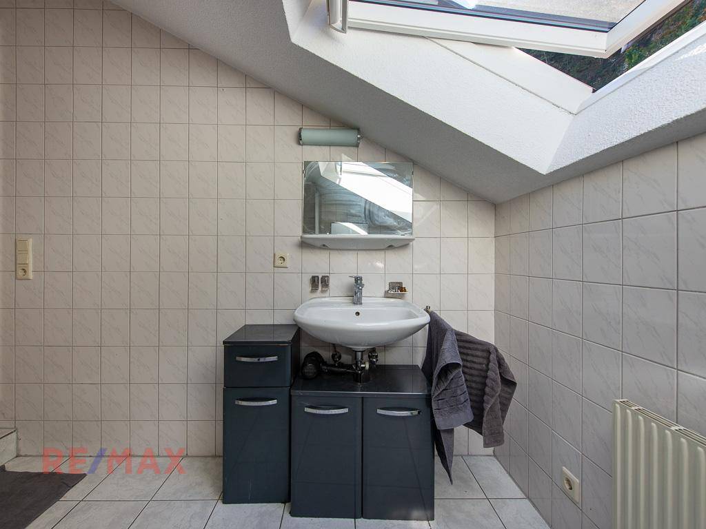Badezimmer im Dachgeschoss mit Waschbecken, Spiegelschrank und Dachfenster.