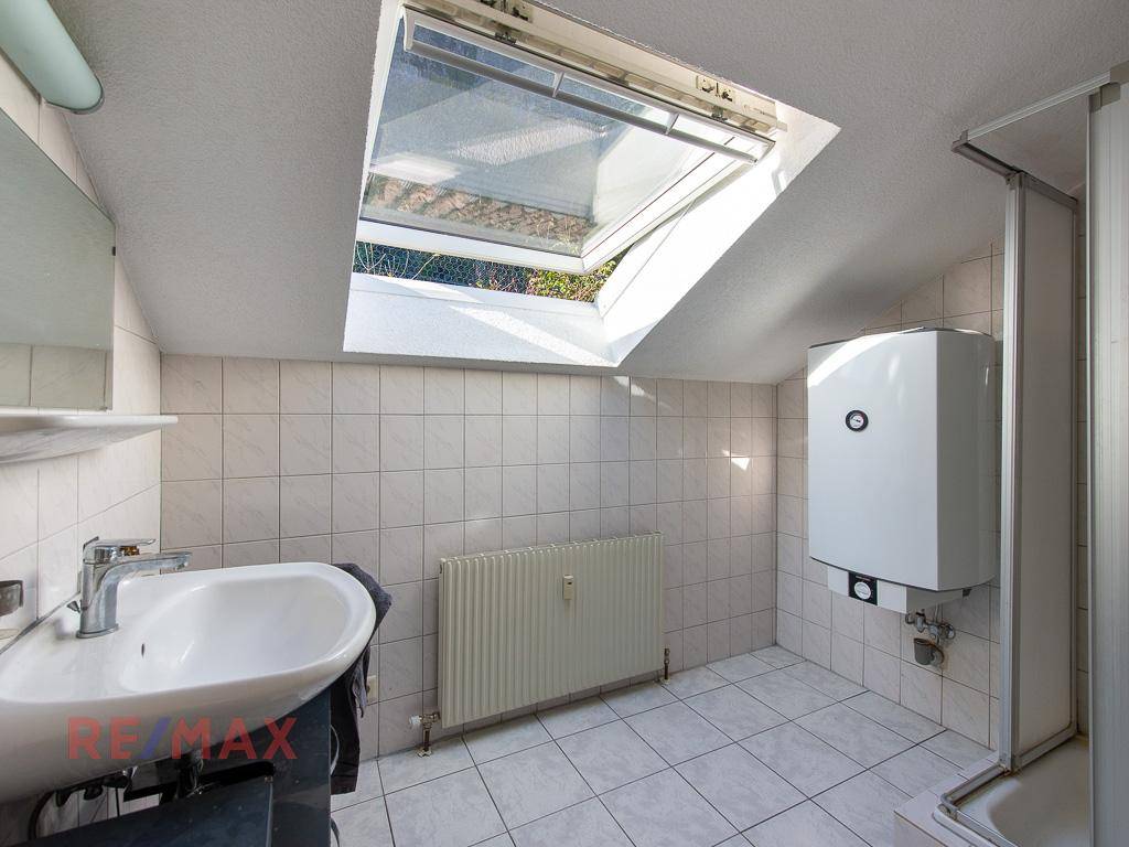 Helles Badezimmer im Dachgeschoss mit Dachfenster, Dusche und Waschbecken.
