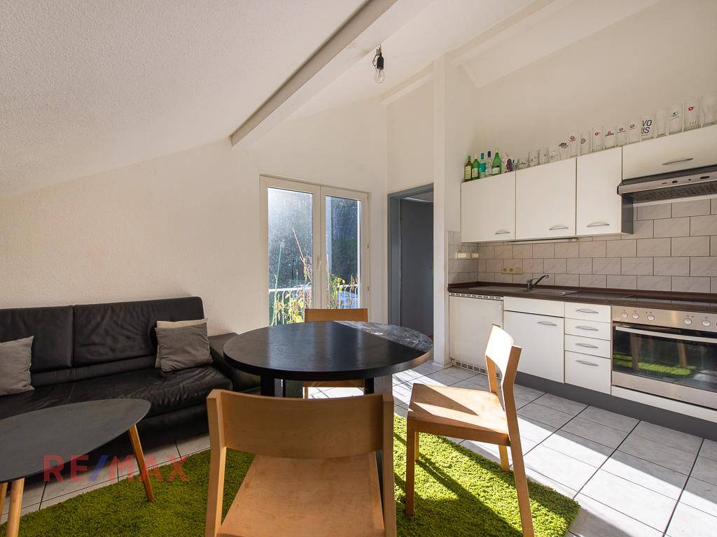 Helles Wohnzimmer mit Küchenzeile, Esstisch und Zugang zu einem kleinen Balkon.