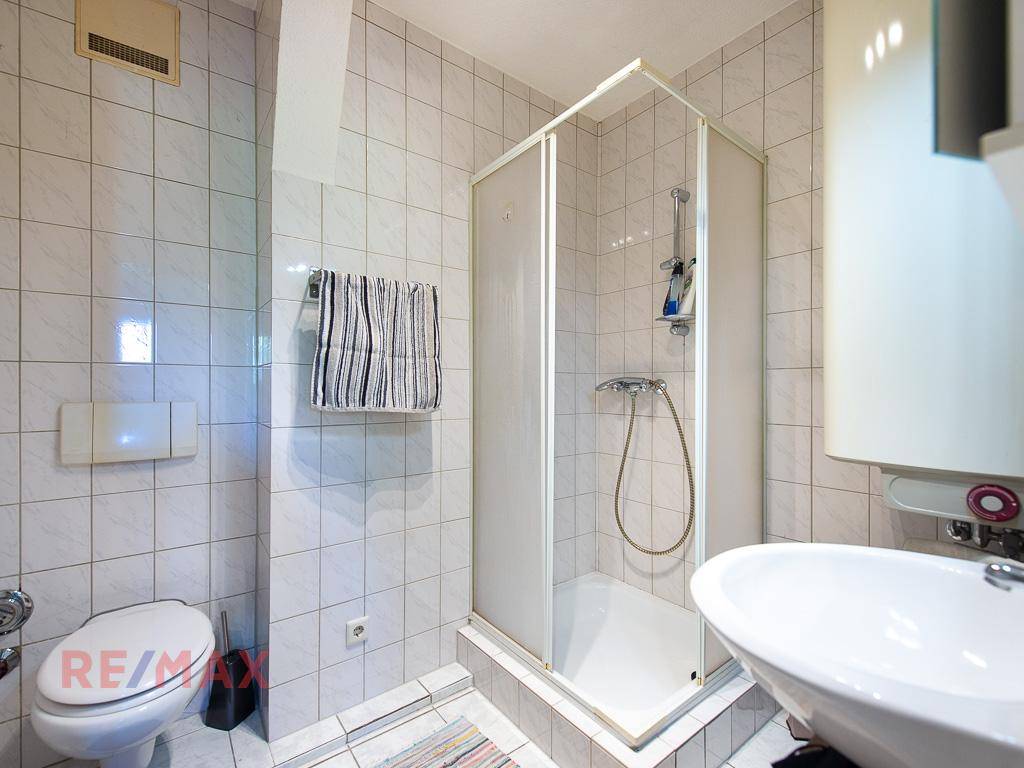 Badezimmer mit Duschkabine, WC und Waschbecken, komplett gefliest in Weiß.