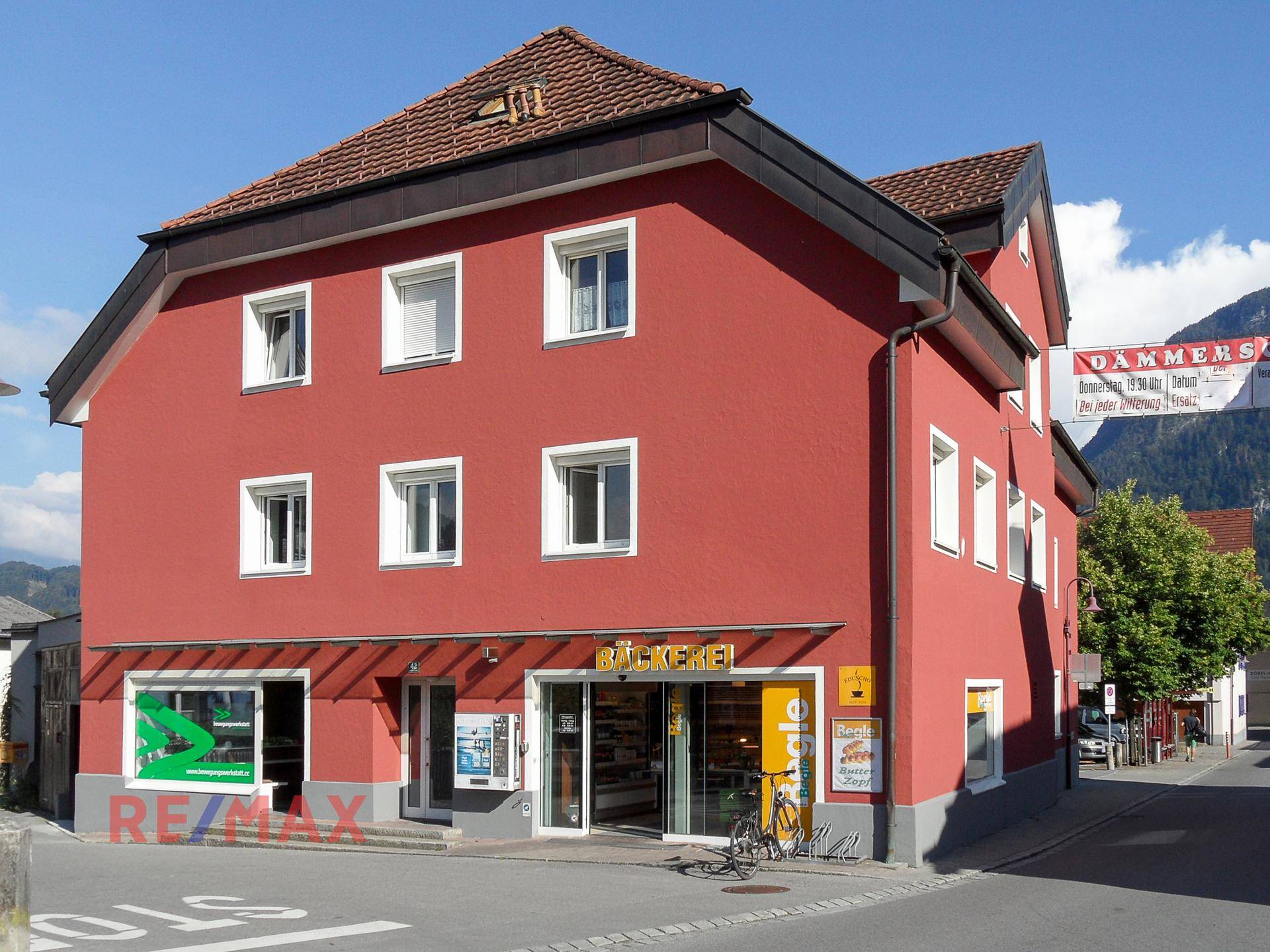 Rotes Gebäude mit Bäckerei im Erdgeschoss und traditionellem Dach in sonniger Umgebung.
