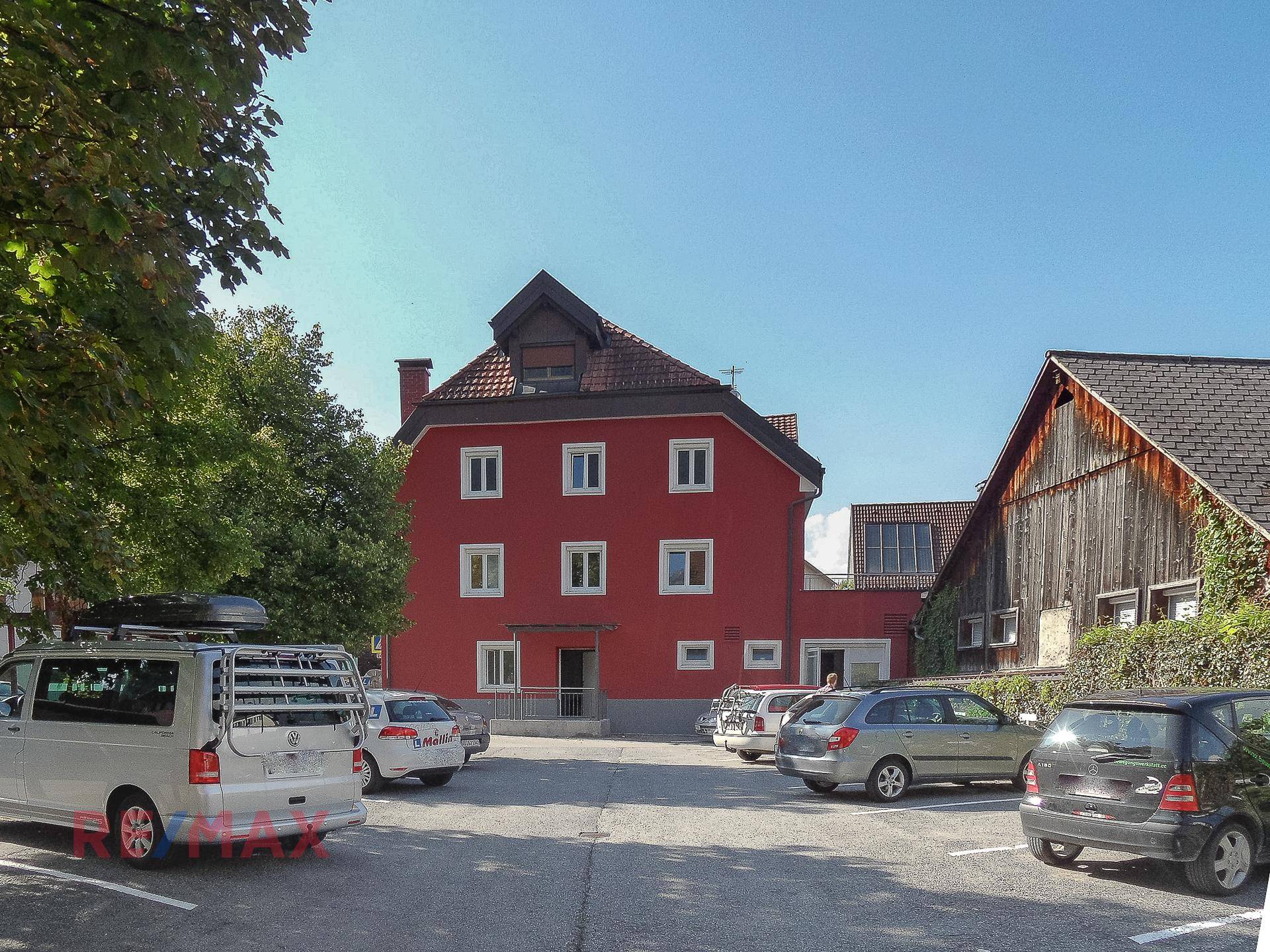 Rückseite des roten Gebäudes mit Parkplatz und angrenzenden traditionellen Holzgebäuden.