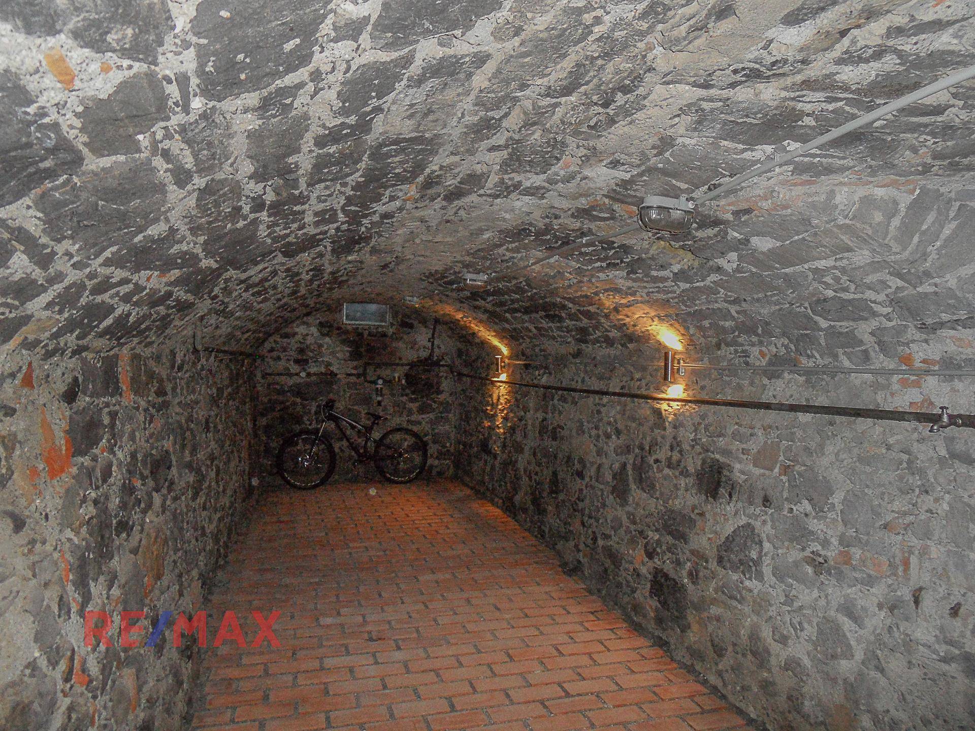 Historischer Gewölbekeller mit Steinmauern und Ziegelboden, beleuchtet von Wandlampen.
